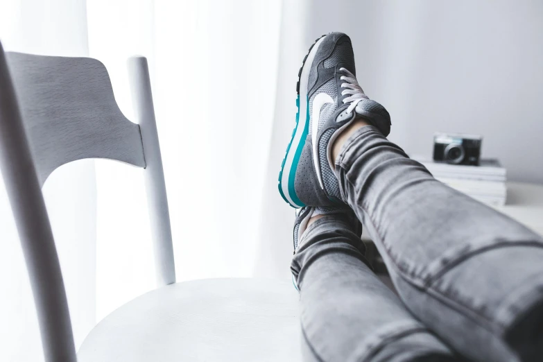 a person sitting on a chair with their feet up, trending on pexels, running shoes, grey and blue theme, on a white table, grey clothes