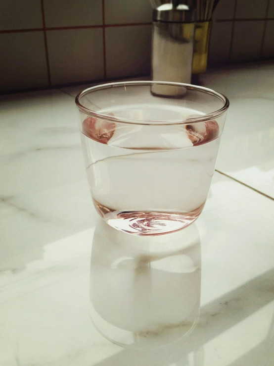 a glass of water sitting on top of a counter, by Eizan Kikukawa, light pink, phone photo, soft light - n 9, hyper realist