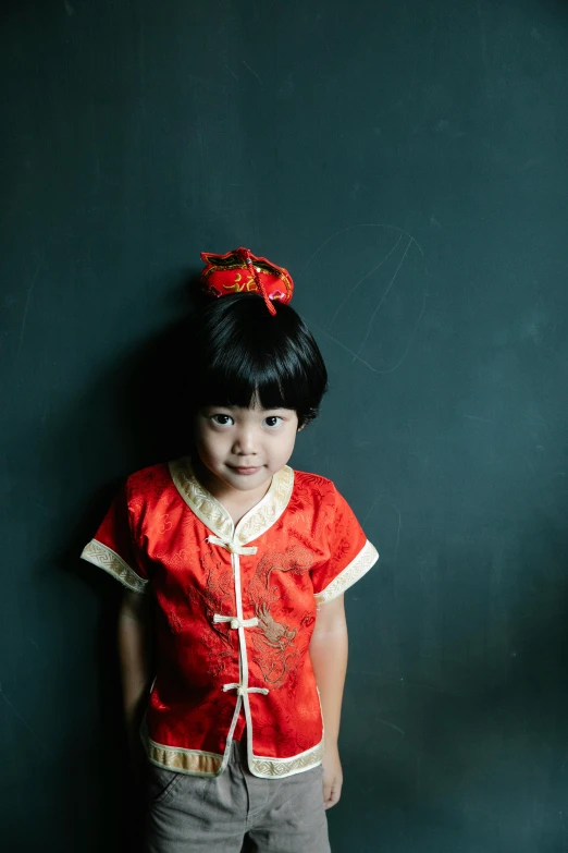 a little girl standing in front of a black wall, a portrait, inspired by Xie Huan, pexels contest winner, wearing festive clothing, plain background, 15081959 21121991 01012000 4k, medium format. soft light