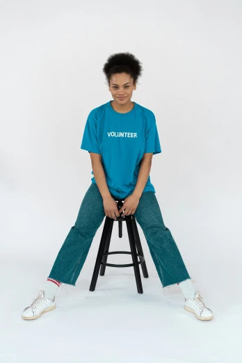 a woman sitting on a stool wearing a volunteer t - shirt, curated collections, teal uniform, trending on r/streetwear, jeans pants