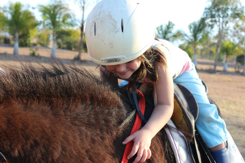 a little girl riding on the back of a brown horse, wearing a helmet, sun coast, amanda lilleston, head down