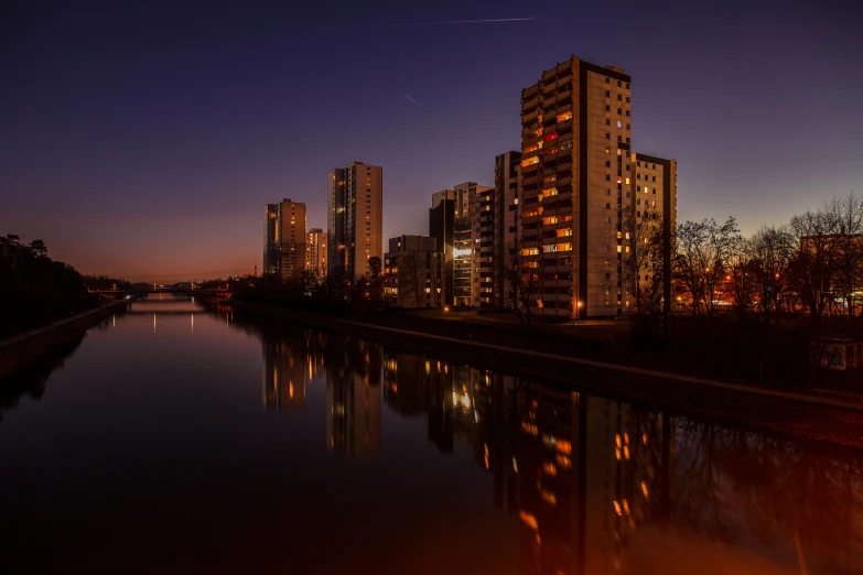 a river running through a city next to tall buildings, by Mathias Kollros, pexels contest winner, hyperrealism, calm evening, habitat 67, portait image, nightfall. quiet