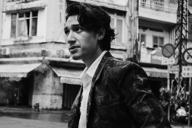 a black and white photo of a man standing in front of a building, a black and white photo, pexels, photorealism, he looks like tye sheridan, avan jogia angel, in an old 1950s leather jacket, portait photo profile picture