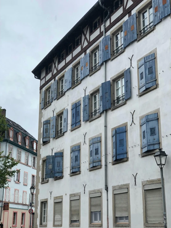 a white building with blue shutters on the windows, inspired by Karl Stauffer-Bern, gray skies, viral image, as well as scratches, square