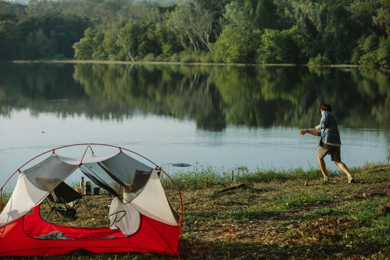 a red and white tent sitting next to a body of water, hurufiyya, camping, person in foreground, jungle setting, walking