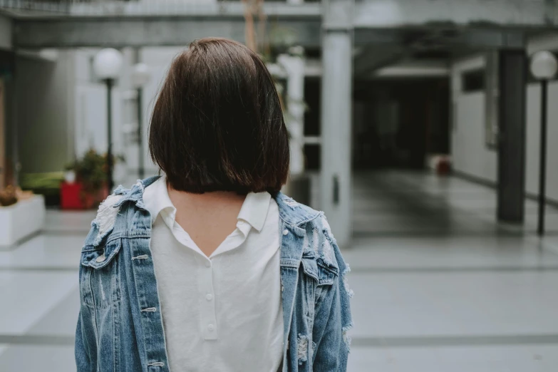 a woman in a white shirt and denim jacket, trending on pexels, standing with her back to us, background image, chin-length hair, candid photo