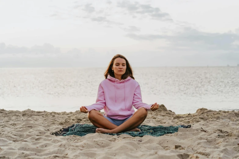 a woman is meditating on the beach, a portrait, by Alice Mason, pexels, wearing a pink hoodie, portrait sophie mudd, full-body, greta thunberg