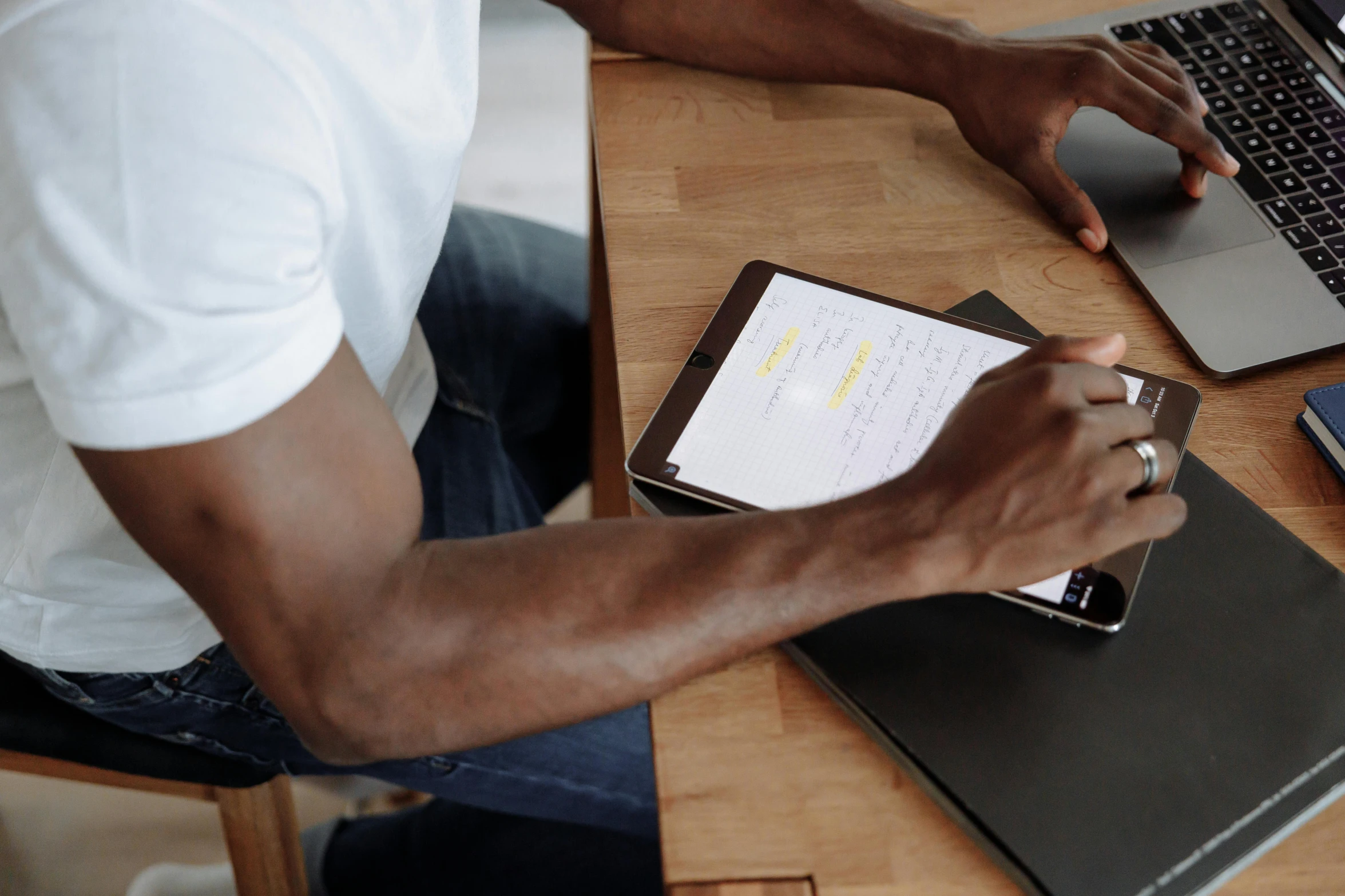 a man sitting at a table with a laptop and a tablet, by Carey Morris, pexels contest winner, emmanuel shiru, holding a clipboard, hands on counter, thumbnail