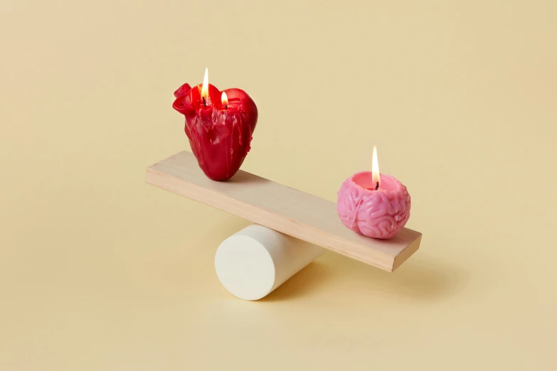 a couple of candles sitting on top of a piece of wood, a surrealist sculpture, inspired by Marina Abramović, vanitas, featuring pink brains, flaming heart, miniature product photo, brightly coloured