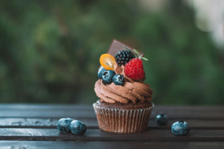 a cupcake sitting on top of a wooden table, pexels contest winner, berries, chocolate frosting, background image, eating outside