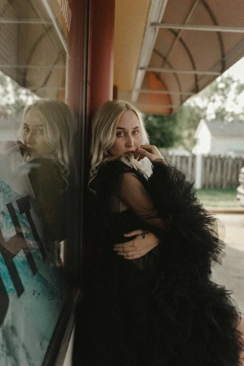 a woman standing in front of a window talking on a cell phone, by Winona Nelson, pexels contest winner, realism, feather boa, portrait of kim petras, leaning on door, dressed in black