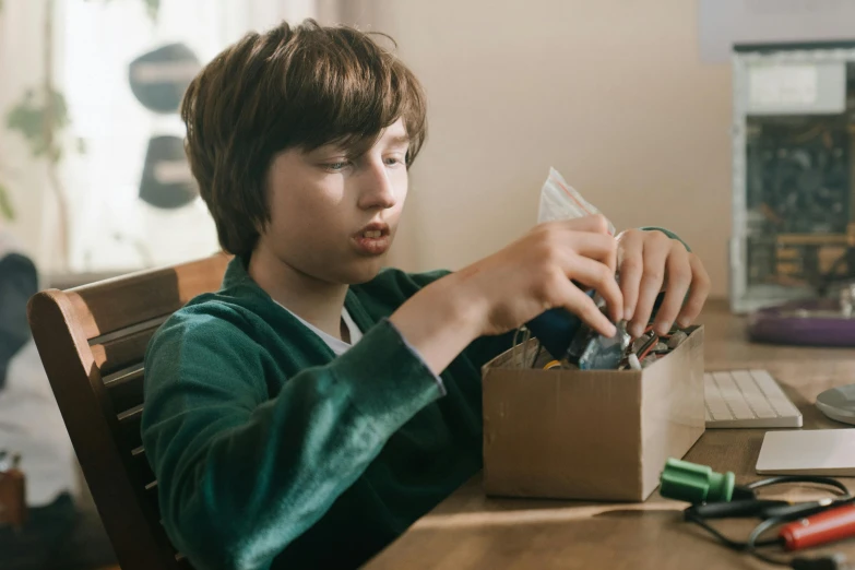 a boy sitting at a table in front of a computer, box cutter, toy package, carefully crafted, thumbnail