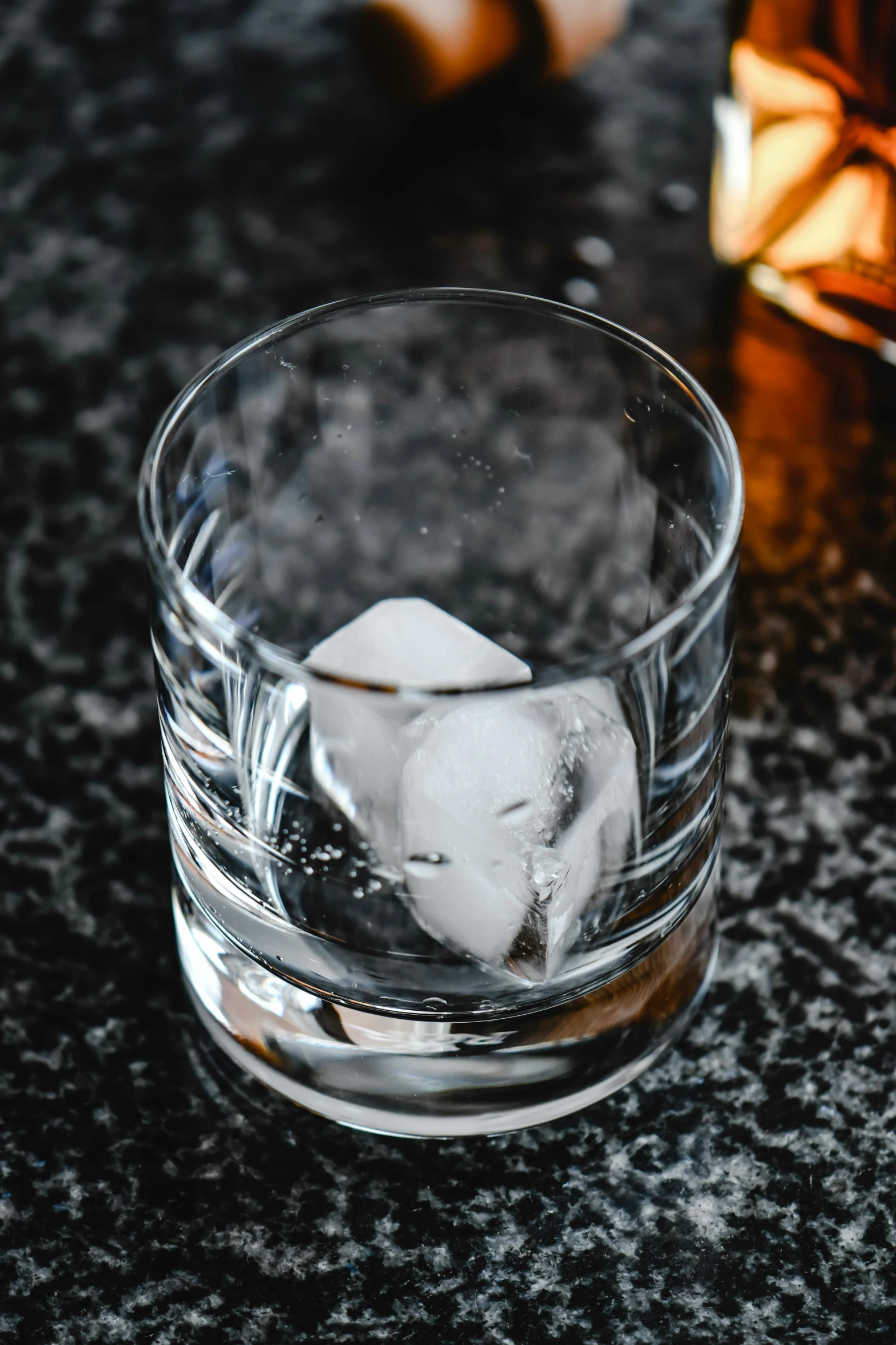 a glass filled with ice next to a bottle of whiskey, unsplash, floating stones, medium format, grey, while marble