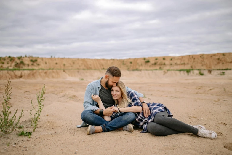 a man and woman sitting on top of a sandy beach, a portrait, by Lee Loughridge, pexels contest winner, cuddly, avatar image, badlands, maternal photography 4 k