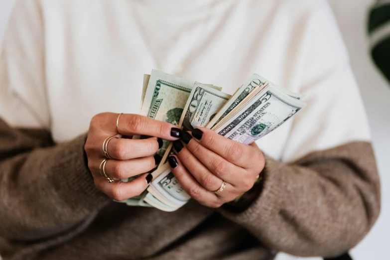 a woman holding a bunch of money in her hands, by Julia Pishtar, pexels contest winner, instagram post, carson ellis, cozy aesthetic, ad image