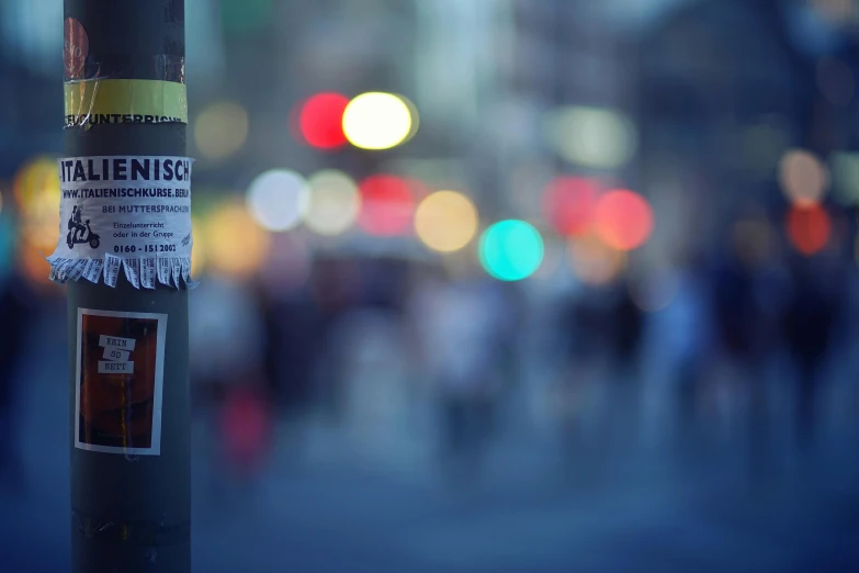 a sticker on a pole on a city street, a picture, by Niko Henrichon, unsplash, happening, hasselblad film bokeh, missing poster, nightlight, people out of focus