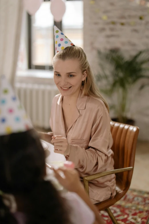 a woman sitting at a table with a birthday hat on, pexels contest winner, happening, two girls, low quality footage, sophisticated young woman, wearing simple robes