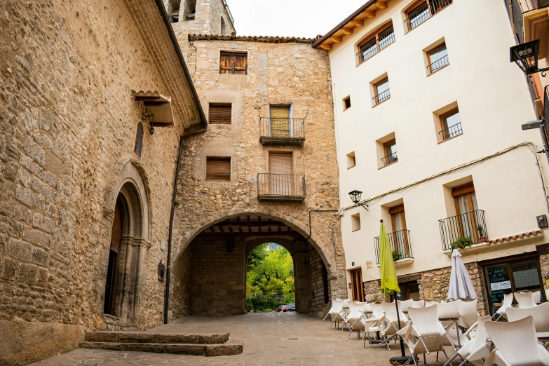 a couple of white chairs sitting on top of a cobblestone street, inspired by Luis Paret y Alcazar, pexels contest winner, romanesque, circular gate in a white wall, thumbnail, monserrat gudiol, massive arch
