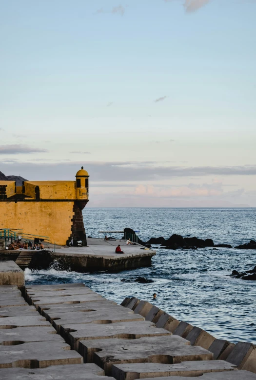 a man riding a skateboard down a sidewalk next to the ocean, a picture, inspired by Juan de Valdés Leal, renaissance, small castle in the distance, azores, at dusk at golden hour, small dock