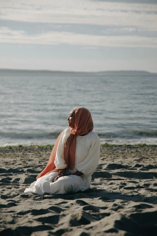 a woman sitting on top of a sandy beach, inspired by Khalil Gibran, unsplash, renaissance, white hijab, seattle, covered in coral, view from the side