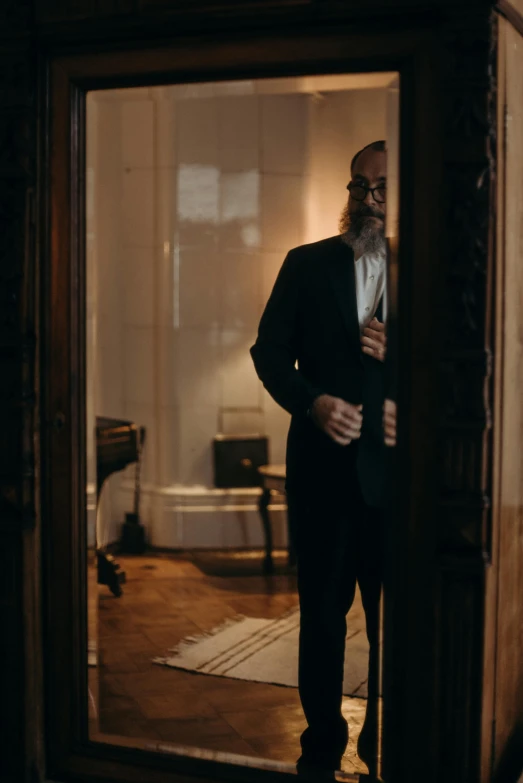 a man in a suit standing in a doorway, an album cover, inspired by George Jamesone, unsplash, baroque, jewish young man with glasses, indoor scene, 2 0 2 1 cinematic 4 k framegrab, long beard