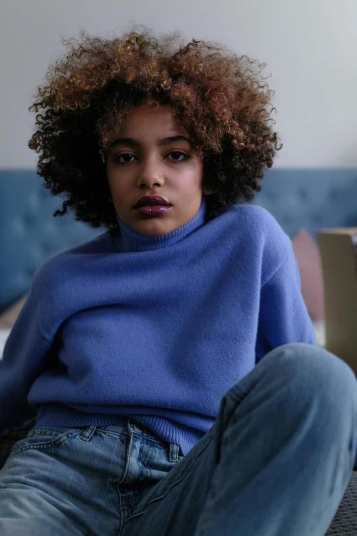 a woman with curly hair sitting on a couch, inspired by Theo Constanté, trending on pexels, renaissance, blue sweater, lilac, wearing turtleneck, at a fashion shoot