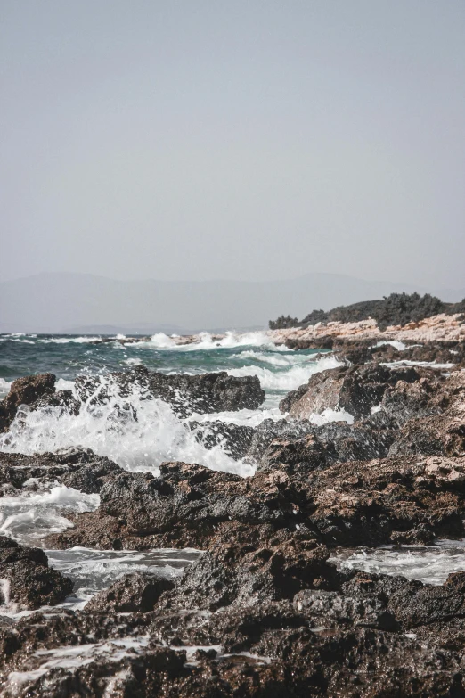 a man standing on top of a rocky beach next to the ocean, les nabis, rough waters, girih, seen from afar, waves and splashes