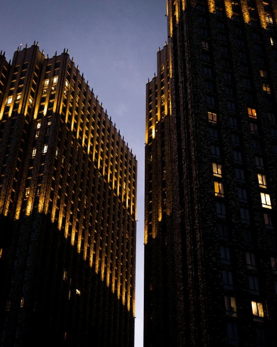 a couple of tall buildings lit up at night, inspired by Ricardo Bofill, unsplash contest winner, stalinist architecture, dark deco, beautiful late afternoon, golden towers