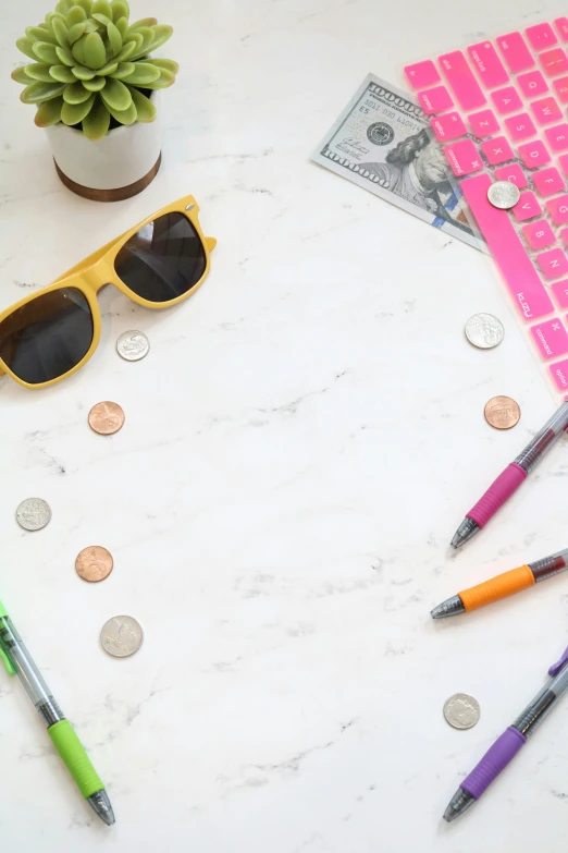 a laptop computer sitting on top of a white table, coins, coloured marker, circular sunglasses, marble table