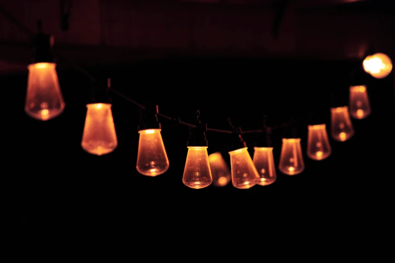 a string of light bulbs hanging from a ceiling, unsplash, romanticism, with orange street lights, hourglass volumetric lighting, glowing firebugs, light cone