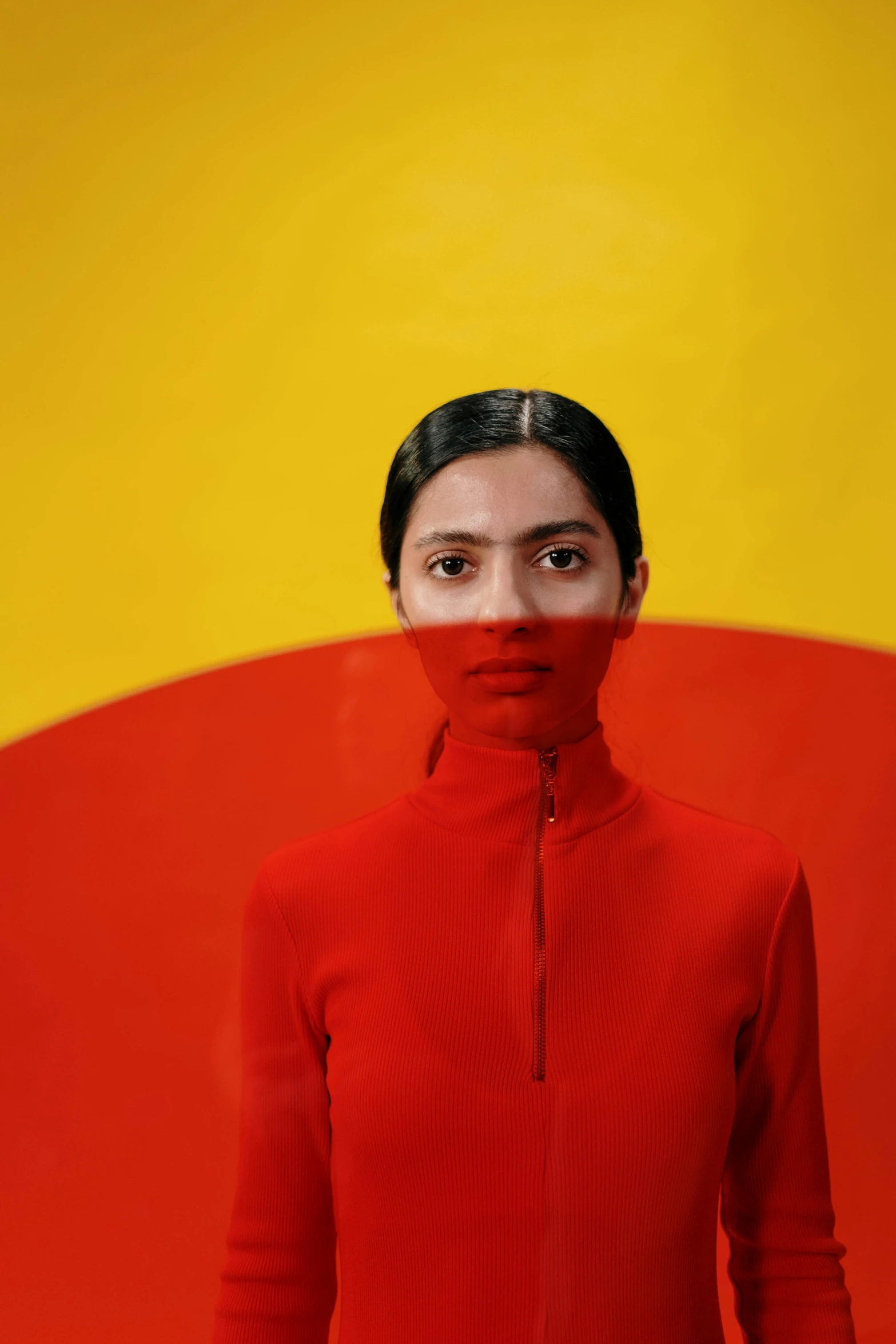 a woman standing in front of a red and yellow wall, inspired by Bert Stern, trending on pexels, color field, wearing turtleneck, symmetrical painted face, freida pinto, on a gray background