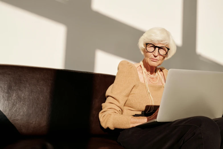 a woman sitting on a couch using a laptop computer, a portrait, pexels, square rimmed glasses, white-haired, frail, a wooden