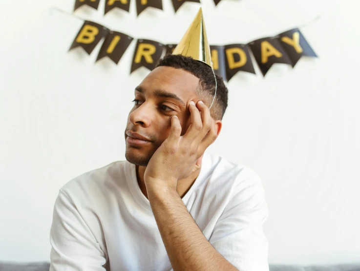 a man sitting on a couch wearing a birthday hat, pexels, 'i'm so tired, man is with black skin, at a birthday party, devastated