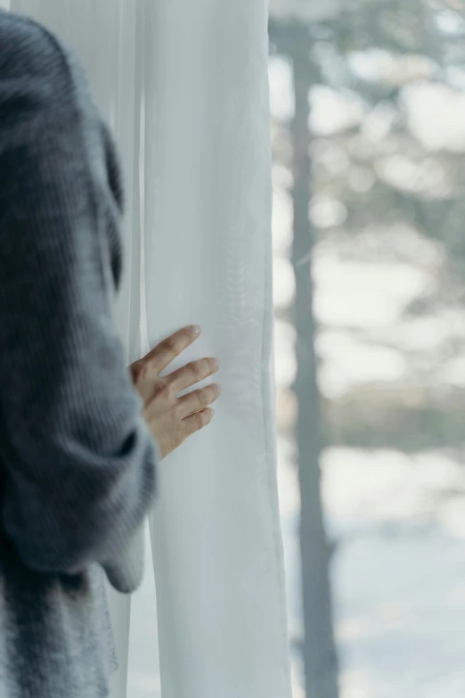 a woman is looking out of a window, by Christen Dalsgaard, pexels contest winner, romanticism, icy cold pale silent atmosphere, holding hand, grey, wearing a white sweater