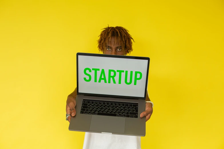 a person holding a laptop with the word startup on it, an album cover, pexels, album art young thug, standing, innovation, wearing yellow croptop