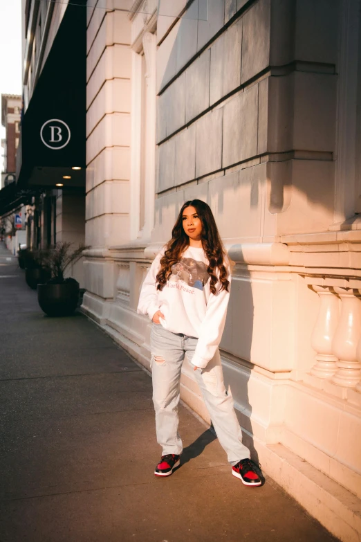a woman standing on a sidewalk in front of a building, white shirt and jeans, ariana grande photography, broad lighting, lizzo