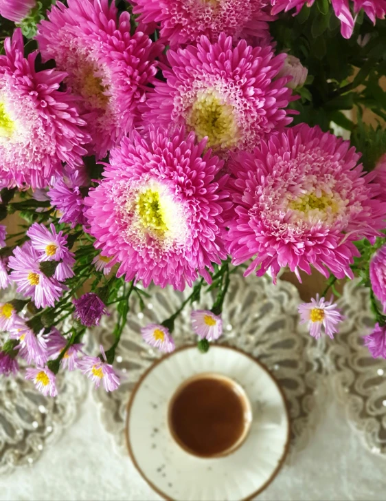 a vase filled with pink flowers next to a cup of coffee, chrysanthemums, zoomed out to show entire image, tea, portrait image