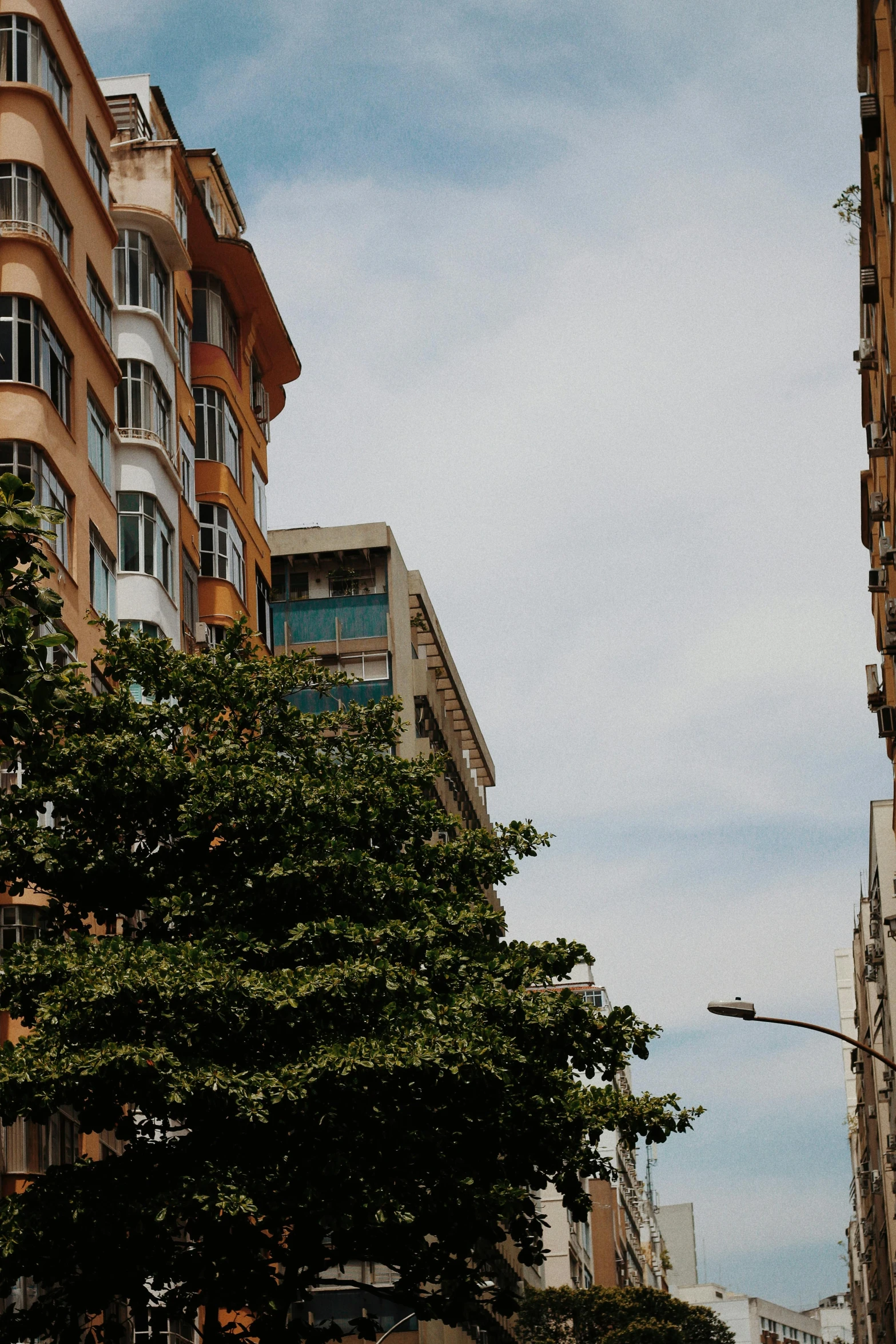 a city street filled with lots of tall buildings, inspired by Óscar Domínguez, unsplash, soviet apartment building, trees in foreground, close up shot from the side, summer day