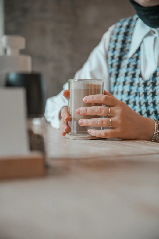 a woman sitting at a table with a glass of water, trending on pexels, hyperrealism, milk and mocha style, sustainable materials, partially cupping her hands, vanilla