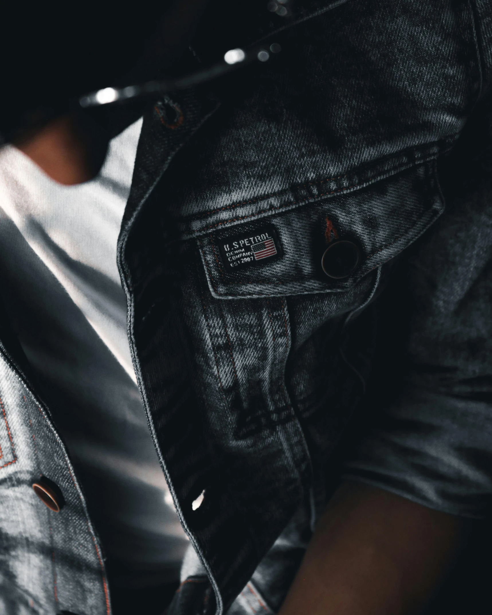 a close up of a person holding a cell phone, wearing a jeans jackets, black and grey, zoomed in, dark photo