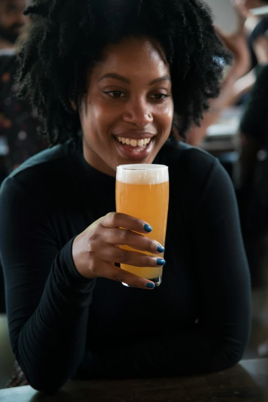 a woman sitting at a table holding a glass of beer, dark skinned, friendly, very consistent, mead