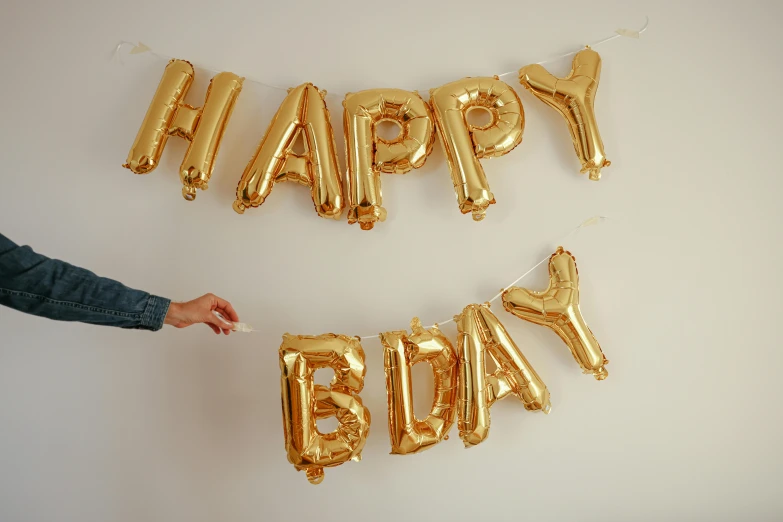 a person holding a balloon that says happy birthday, by Nina Hamnett, happening, brass plated, various sizes, medium wide shot, detailed letters