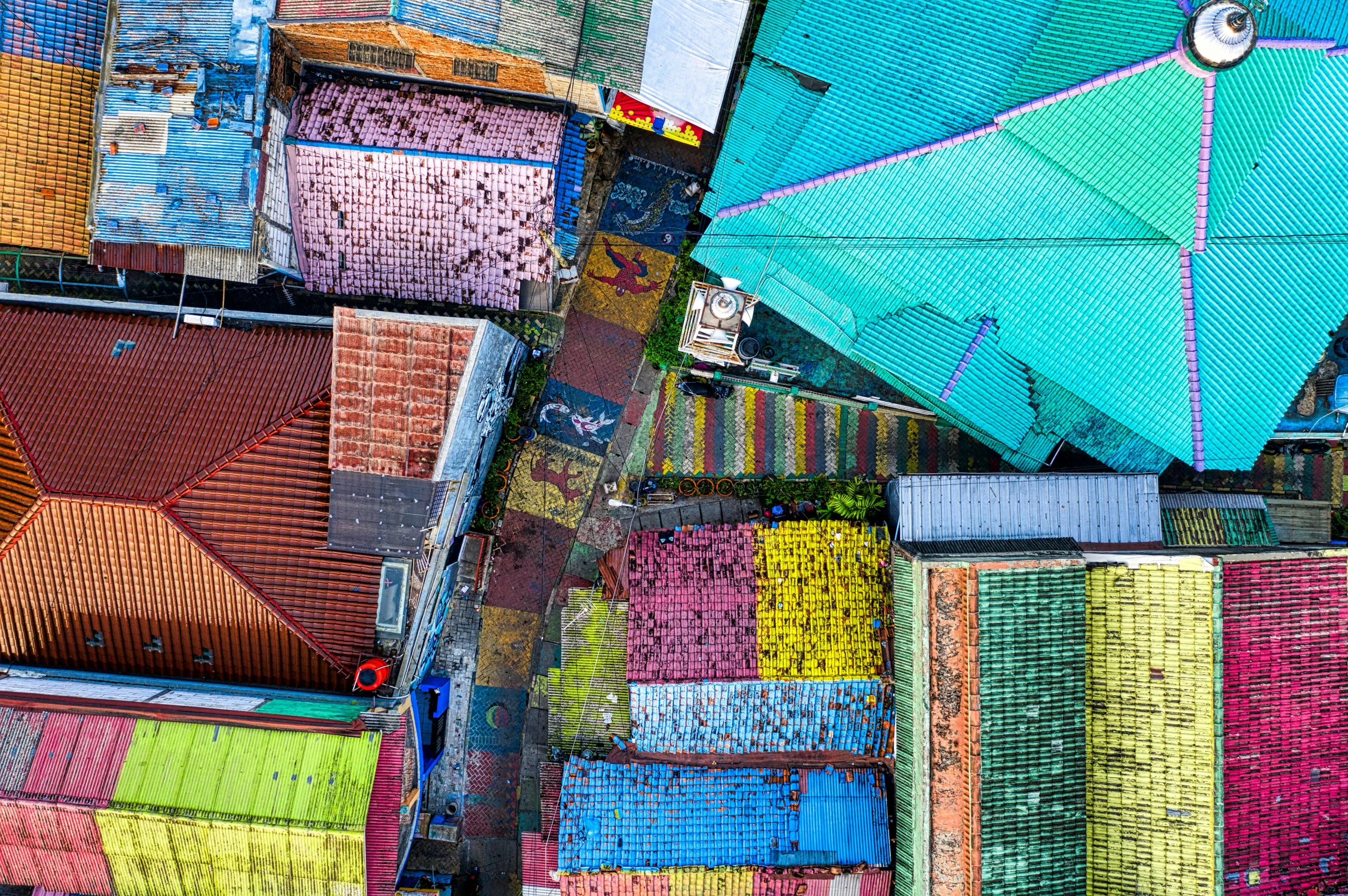 a group of colorful umbrellas sitting on top of a roof, a mosaic, unsplash contest winner, street art, jakarta, color aerial photo drone, back alley, dezeen