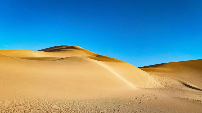 a person riding a snowboard on top of a sandy hill, by Julia Pishtar, unsplash contest winner, art nouveau, panoramic photography, sahara, ultramarine blue and gold, high detail photo of a deserted