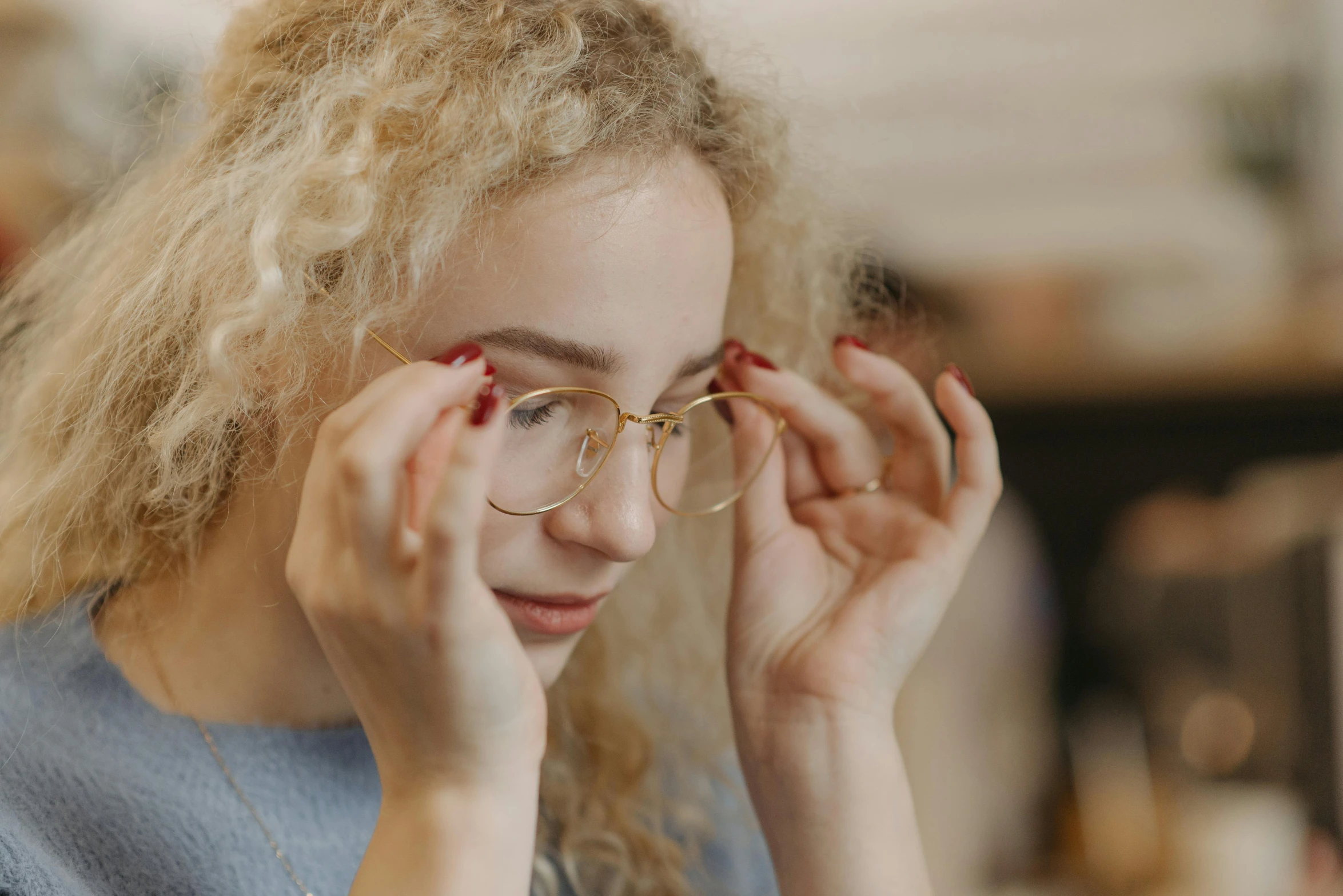 a woman with glasses sitting at a table, a picture, trending on pexels, curly blond, silver small small small glasses, people look into the frame, glasses |