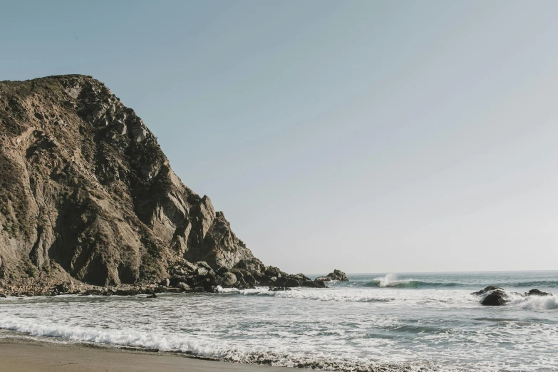 a man riding a surfboard on top of a sandy beach, by Carey Morris, unsplash contest winner, visual art, steep cliffs, hollister ranch, 2 5 6 x 2 5 6 pixels, viewed from the ocean