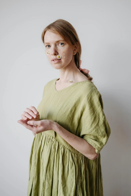 a woman standing in front of a white wall, by Tsuruko Yamazaki, unsplash, renaissance, green tunic, collection product, nursing, with a soft