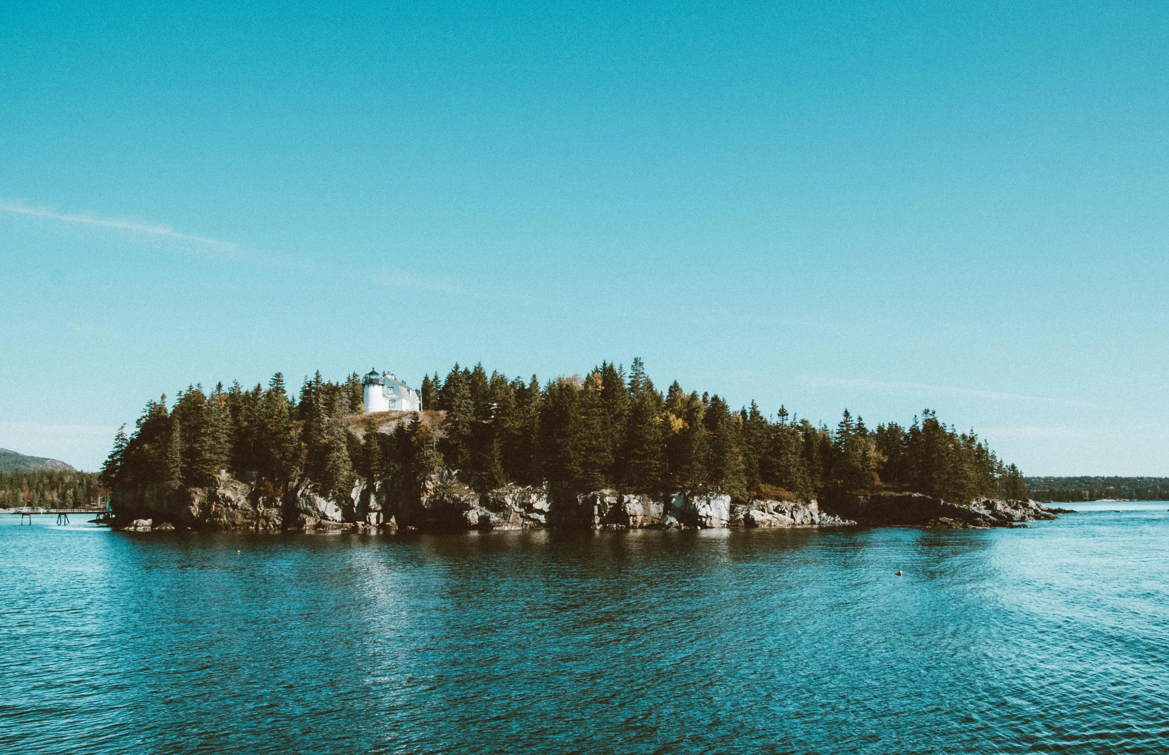 a small island in the middle of a body of water, pexels contest winner, pine trees in the background, bold lighthouse in horizon, maple syrup sea, lake blue