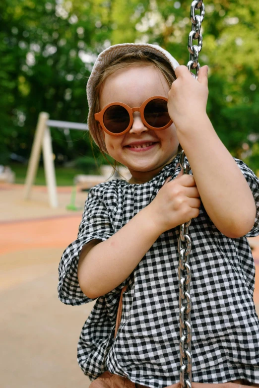 a little girl that is sitting on a swing, wearing orange sunglasses, squares, lookbook, detail shot