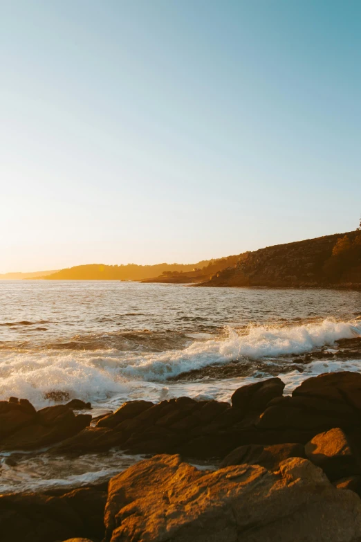 a man riding a surfboard on top of a rocky beach, at the golden hour, hills and ocean, golden hour photograph, no crop